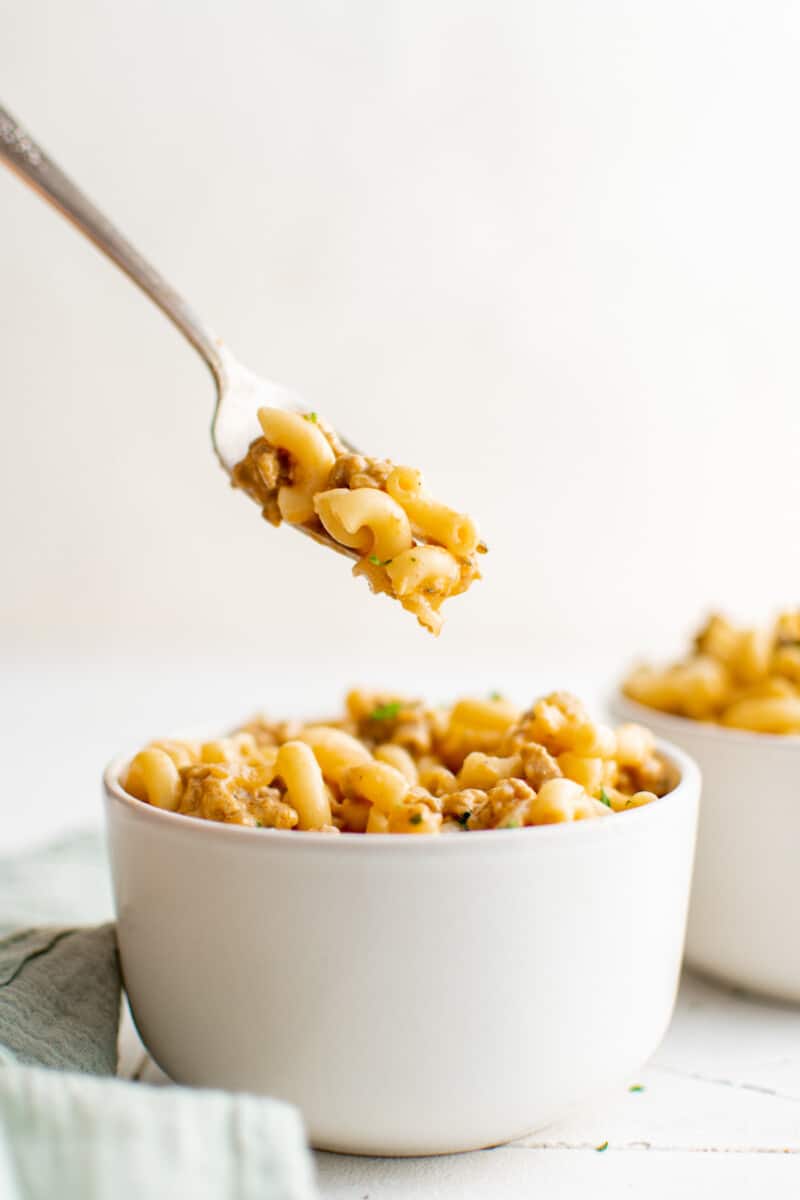 a forkful of hamburger helper hovering above hamburger helper in a white bowl.