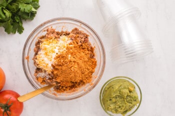 taco seasoning and cream added to refried beans in a glass bowl.
