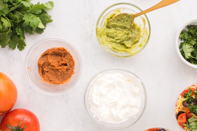 refried beans in a small cup next to bowls of sour cream and guacamole.