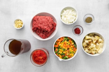 overhead view of ingredients for hamburger soup in white and glass bowls.