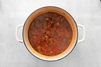 overhead view of broth and tomatoes added to ground beef in a white dutch oven.