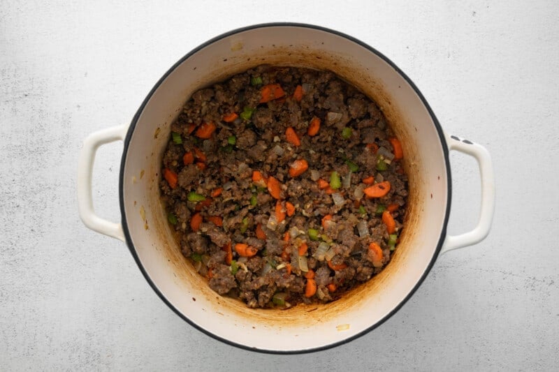 browned sausage and vegetables in a white dutch oven.