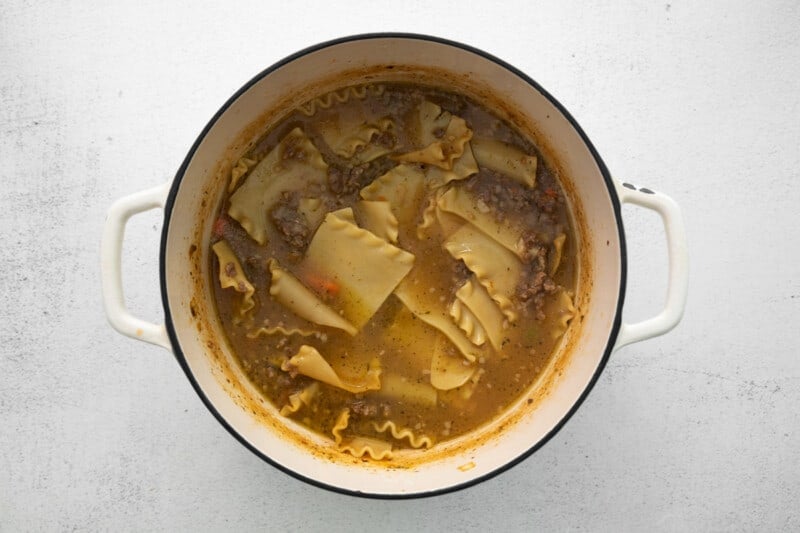 lasagna noodles added to white lasagna soup in a white dutch oven.