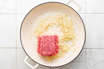 overhead view of raw ground beef added to garlic and onion in a white pan.