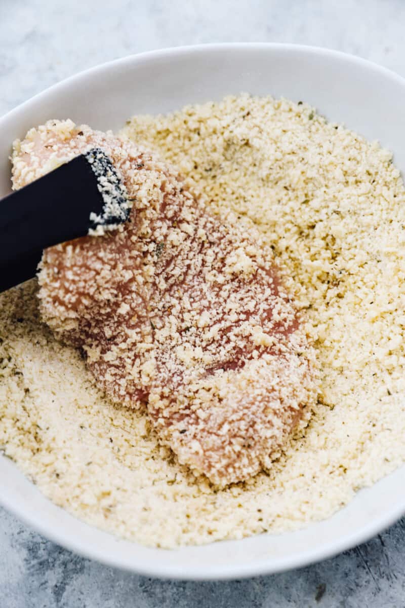 Coating a chicken breast in breadcrumbs.