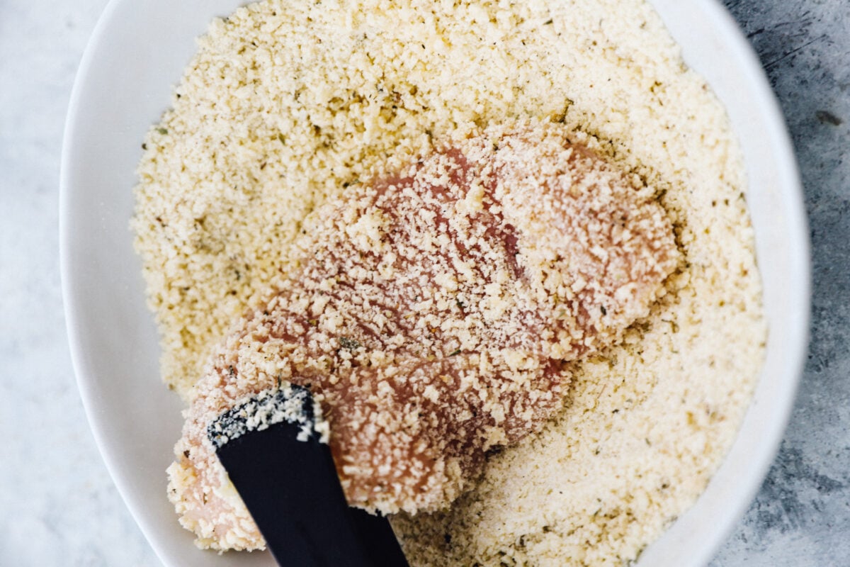Coating a chicken breast in breadcrumbs.
