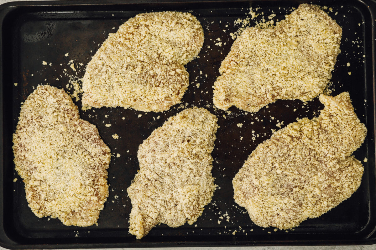 Breaded chicken breasts on a baking pan.