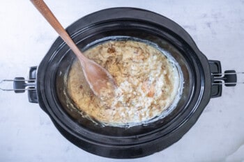 a wooden spoon stirring crockpot chicken and stuffing in a black crockpot.