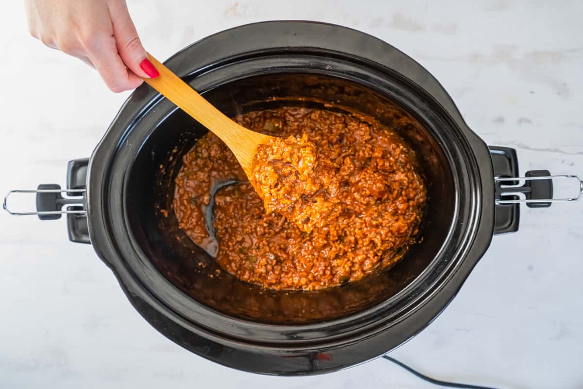 wooden spoon scooping up sloppy Joe mixture out of the slow cooker.