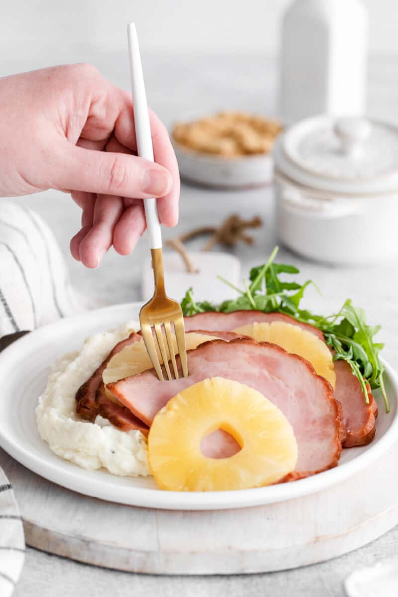 a fork stabbing a slice of instant pot pineapple brown sugar ham on a white plate.