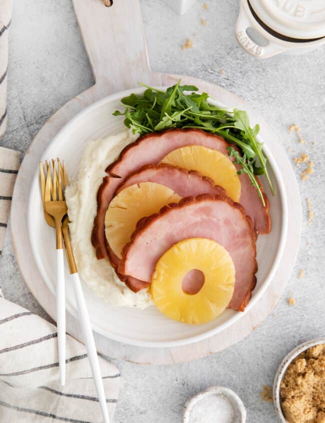 overhead view of instant pot pineapple brown sugar ham on a white plate with a fork and knife.