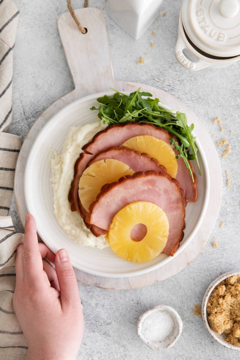 a hand grabbing a plateful of instant pot pineapple brown sugar ham.