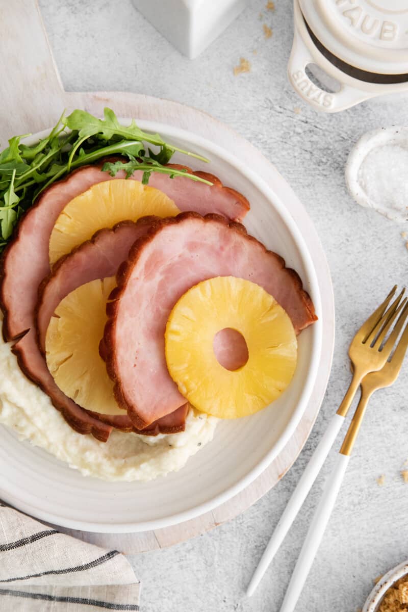 overhead view of instant pot pineapple brown sugar ham on a white plate with a fork and knife.