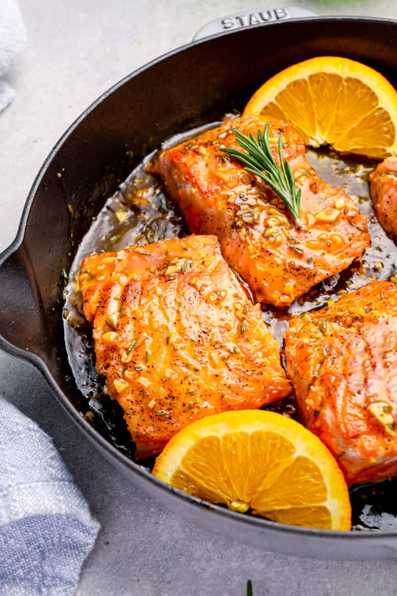 salmon filets in a cast iron skillet, cooking in a a glaze with orange slices