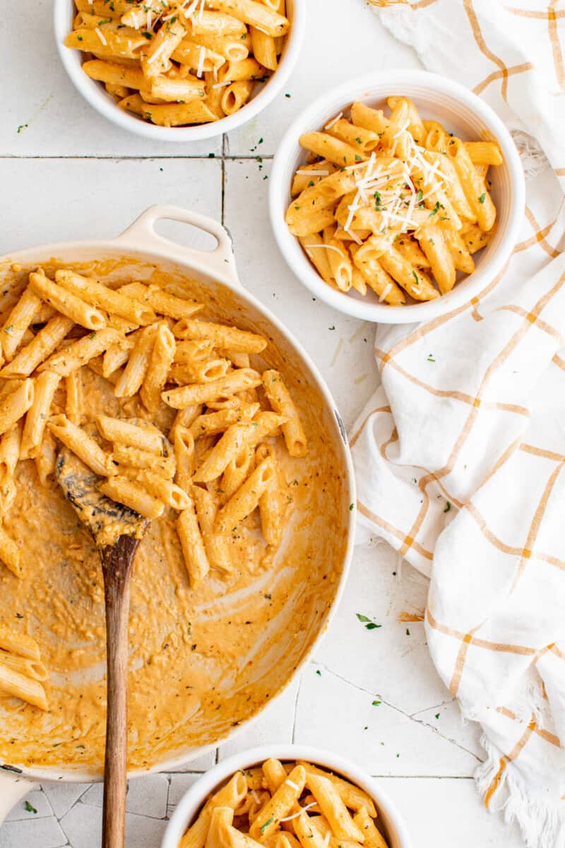 bowls of pasta on a countertop next to a skillet of pasta