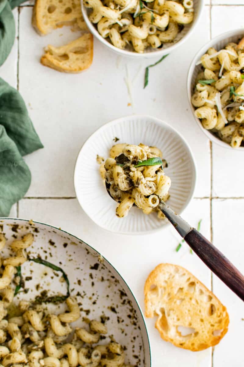 bowls of pasta on a countertop, next to a serving bowl of pasta and pieces of bread