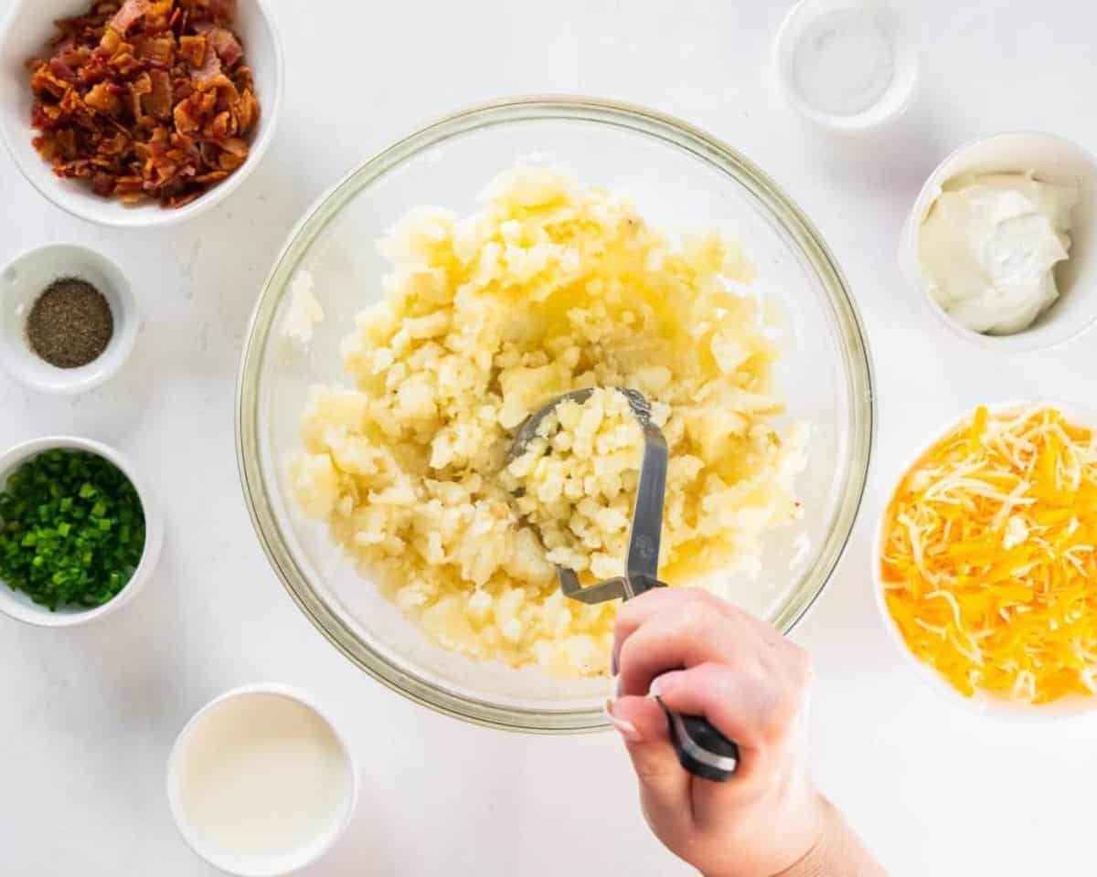 Potato masher mashing potatoes in a glass bowl.