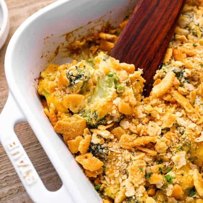 broccoli cheese casserole in a white baking pan with a wooden spoon.