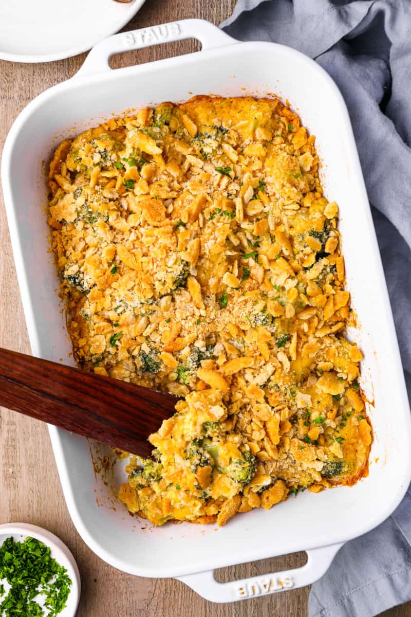 broccoli cheese casserole in a white baking pan with a wooden spoon.