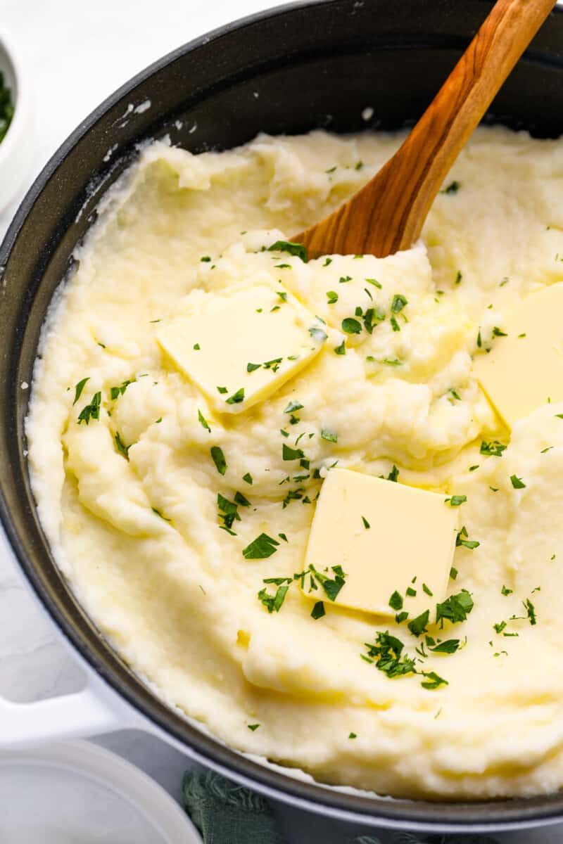 close up of creamy mashed potatoes in a cast iron skillet with a wooden spoon.
