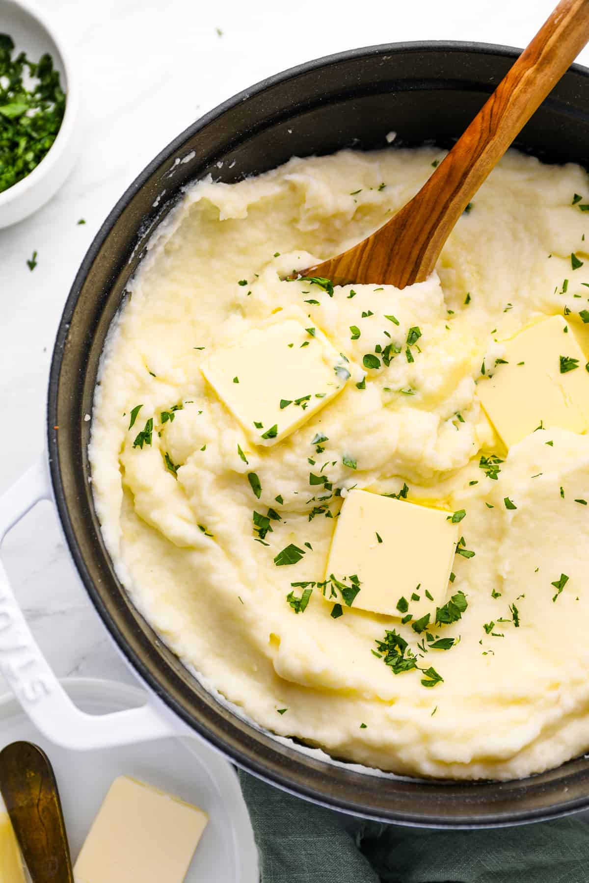 creamy mashed potatoes in a cast iron skillet with a wooden spoon.