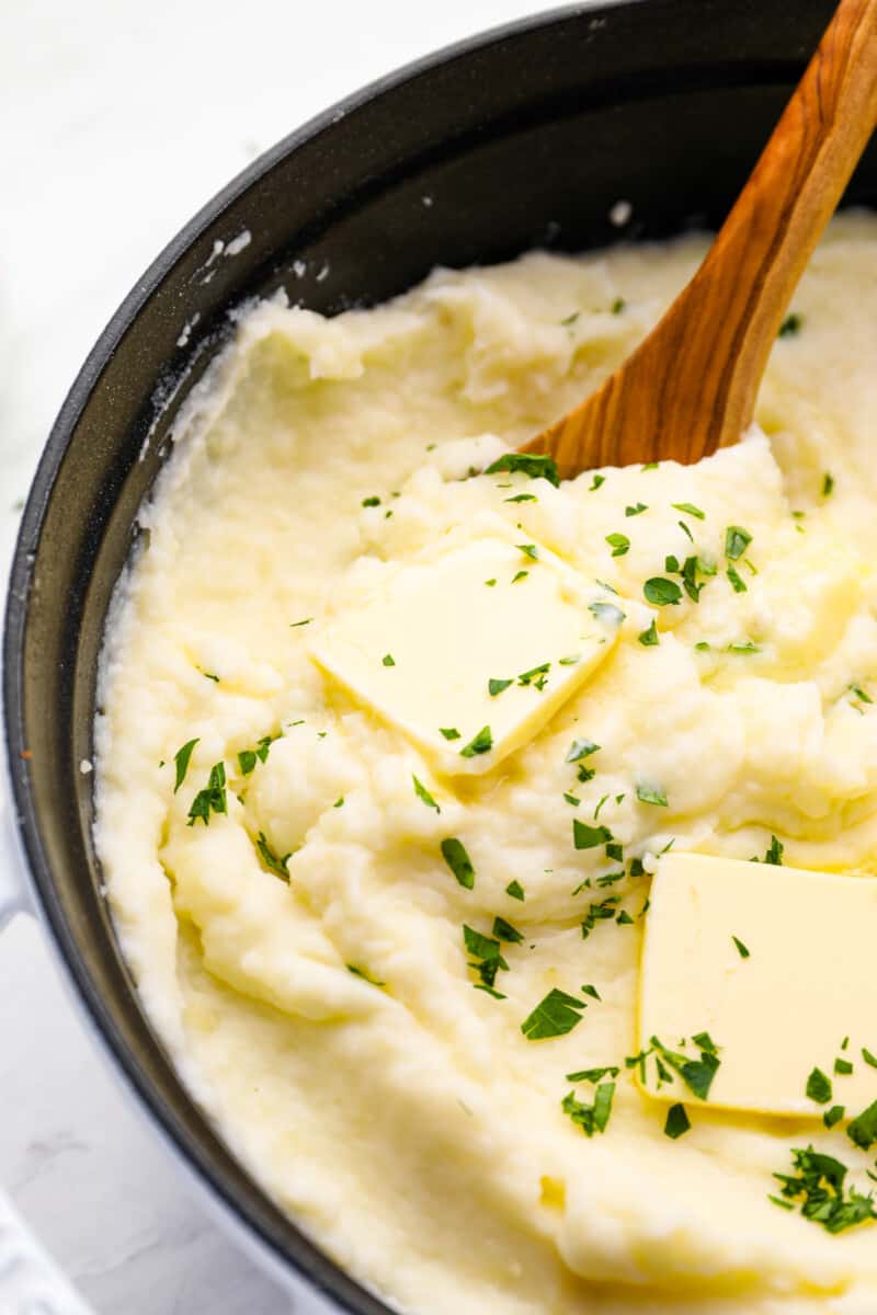 creamy mashed potatoes in a cast iron skillet with a wooden spoon.