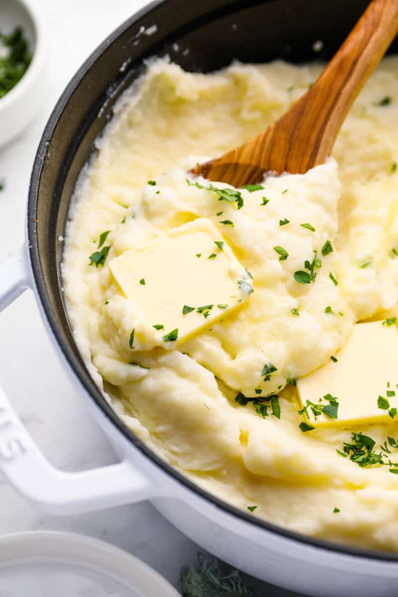 creamy mashed potatoes in a cast iron skillet with a wooden spoon.