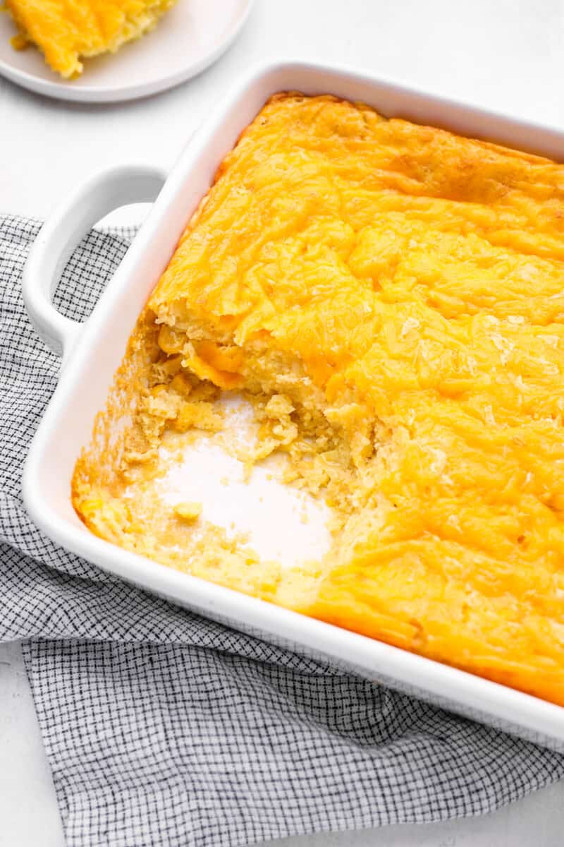corn casserole missing a scoop in a white baking dish.