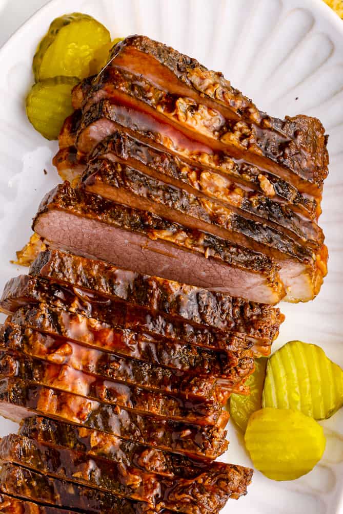 thin slices of brisket on a serving plate with pickles