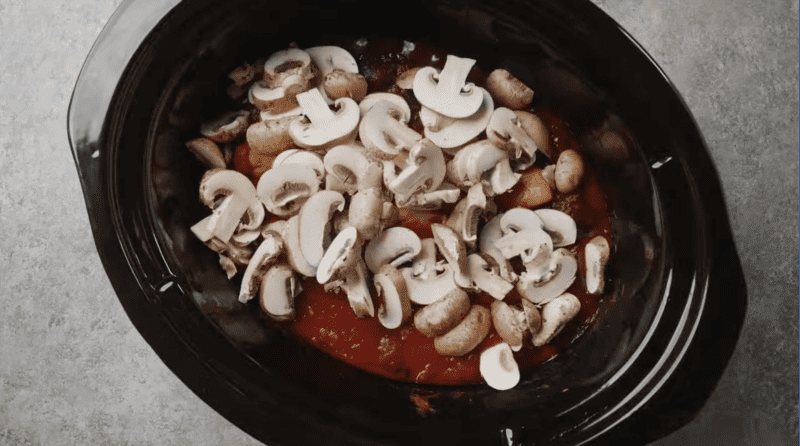 A crockpot filled with mushrooms, tomatoes, and chicken cacciatore.