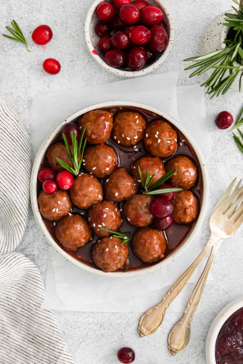 cranberry sauce meatballs in a serving bowl, on a table with forks and cranberries