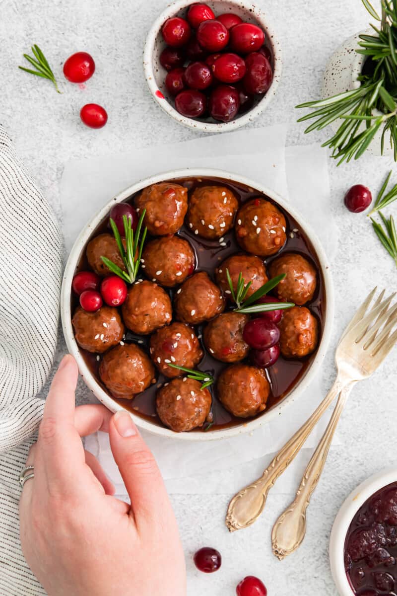 hand reaching towards a bowl of cranberry meatballs