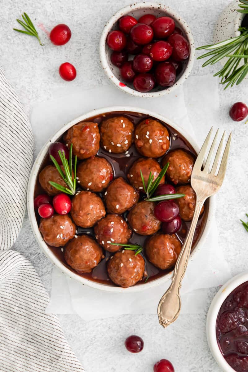 cranberry crockpot meatballs in a serving bowl, next to. bowl of cranberries