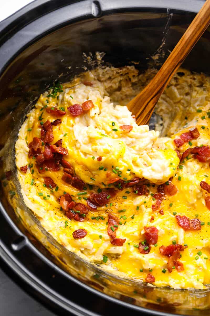 a spoon stirring crockpot cheesy hashbrown potatoes in a crockpot.