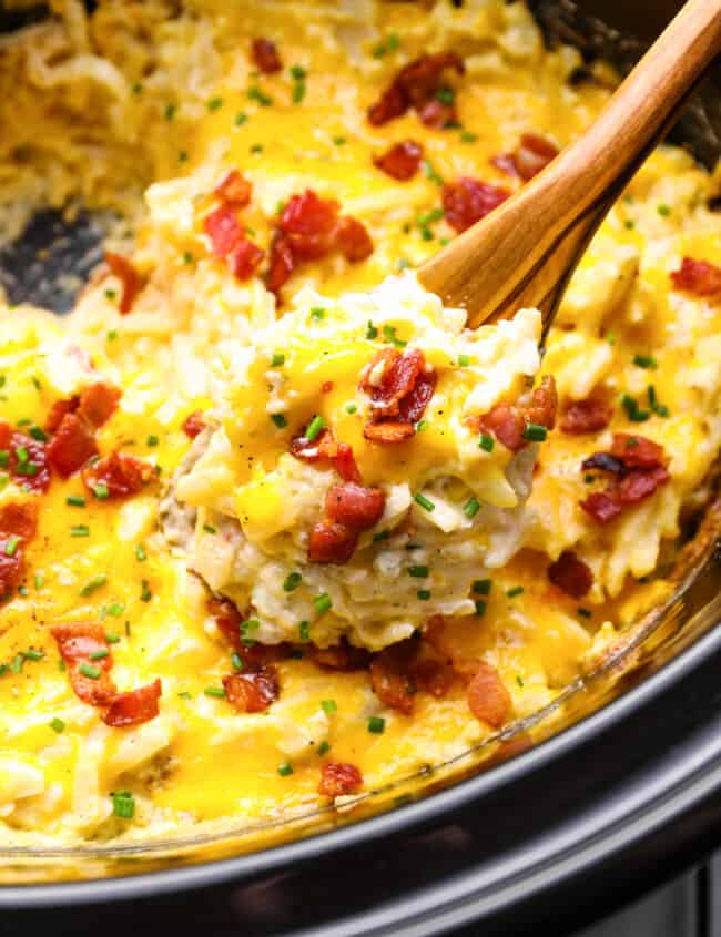 a spoon lifting a scoop of crockpot cheesy hashbrown potatoes out of a crockpot.