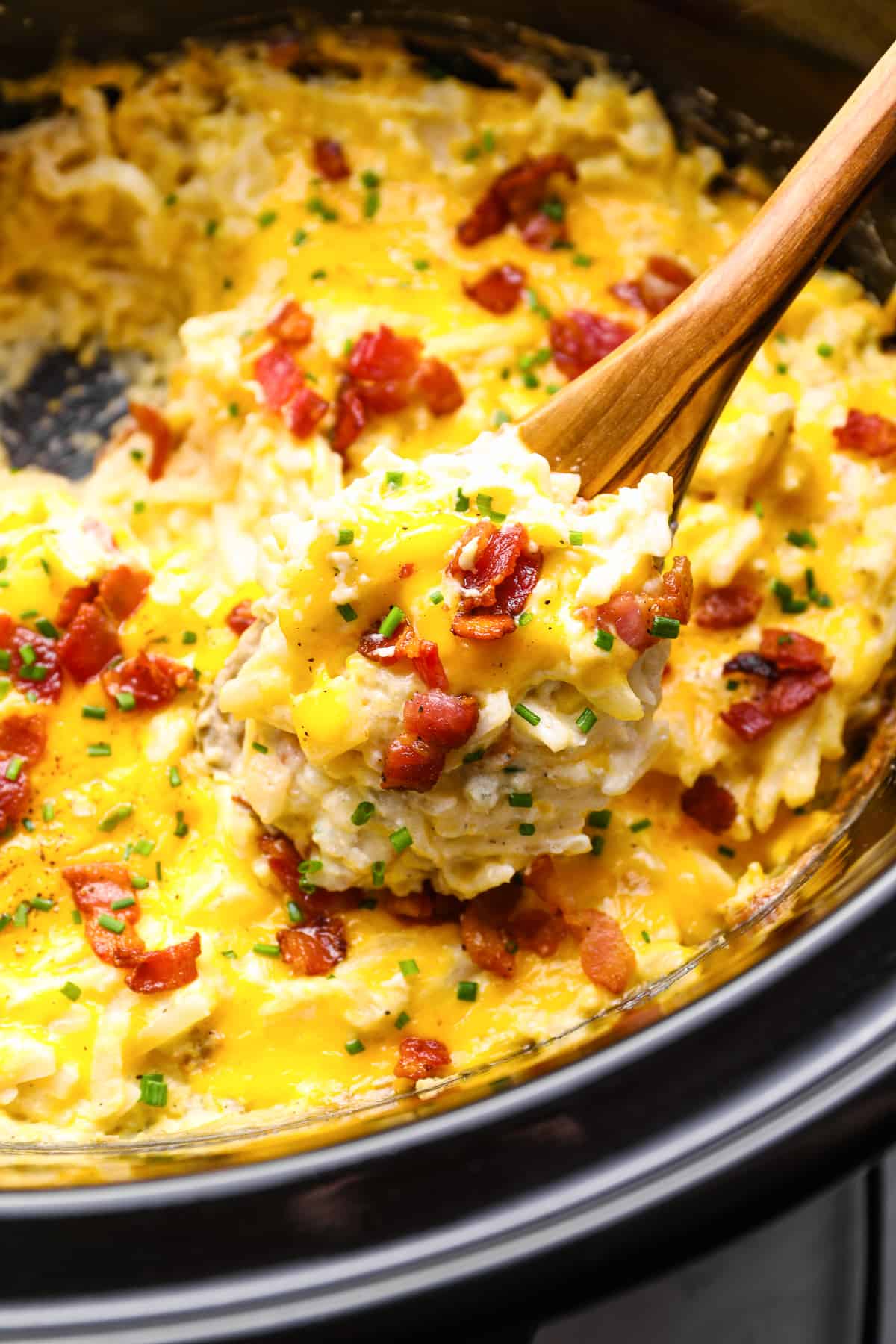 a spoon lifting a scoop of crockpot cheesy hashbrown potatoes out of a crockpot.