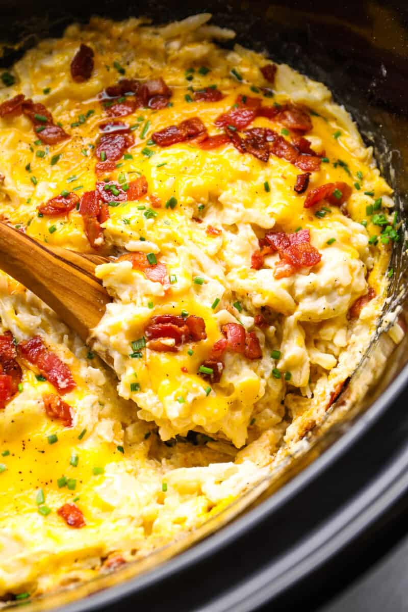 crockpot cheesy hashbrown potatoes in a crockpot with a wooden spoon.