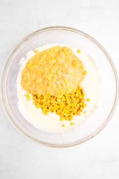 corn kernels and creamed corn added to sour cream mixture for corn casserole in a glass bowl.