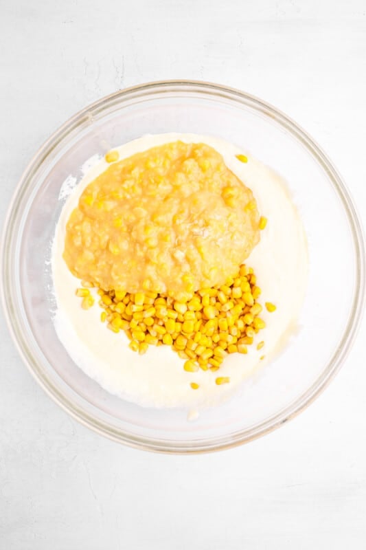 corn kernels and creamed corn added to sour cream mixture for corn casserole in a glass bowl.