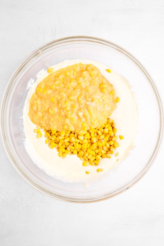 corn kernels and creamed corn added to sour cream mixture for corn casserole in a glass bowl.