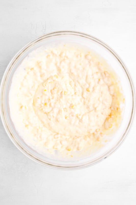 corn muffin mix added to corn casserole in a glass bowl.