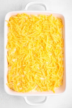 corn casserole mixture in a white baking dish topped with cheese.
