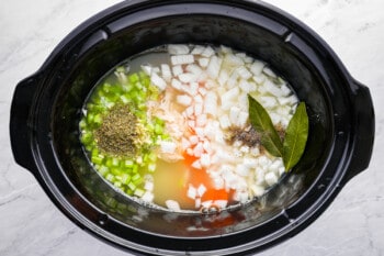 chopped veggies and soup ingredients in the bowl of a crockpot