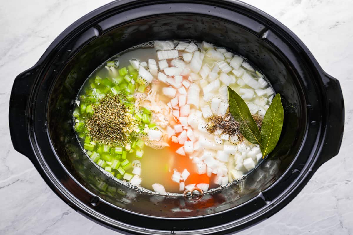 chopped veggies and soup ingredients in the bowl of a crockpot.