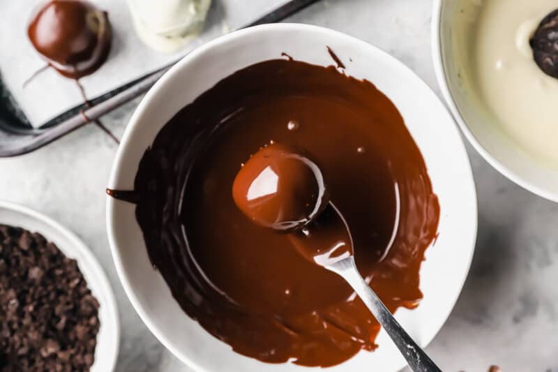 a fork dipping an oreo ball into melted chocolate in a white bowl.