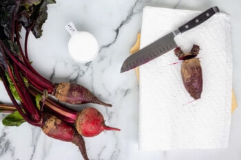 overhead view of a beet on a white cutting board with a knife.