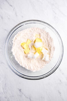 overhead view of flour with cubes of butter and shortening in a glass bowl.