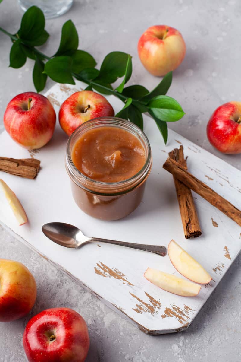 jar of instant pot apple butter on a board, surround by apples and cinnamon
