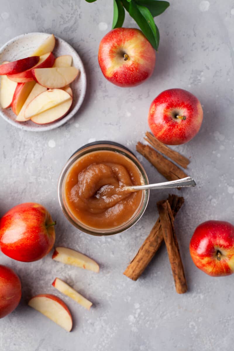 overhead view of a jar of apple butter, surrounded by apples, cinnamon sticks, and apple slices