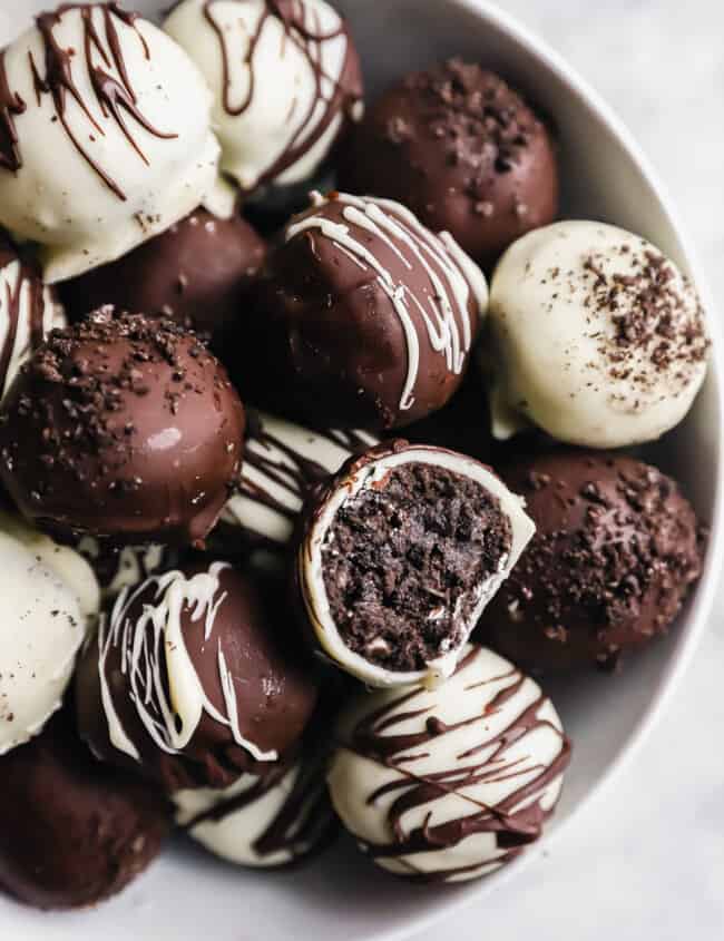 a bitten oreo ball resting on a pile of oreo balls in a white bowl.